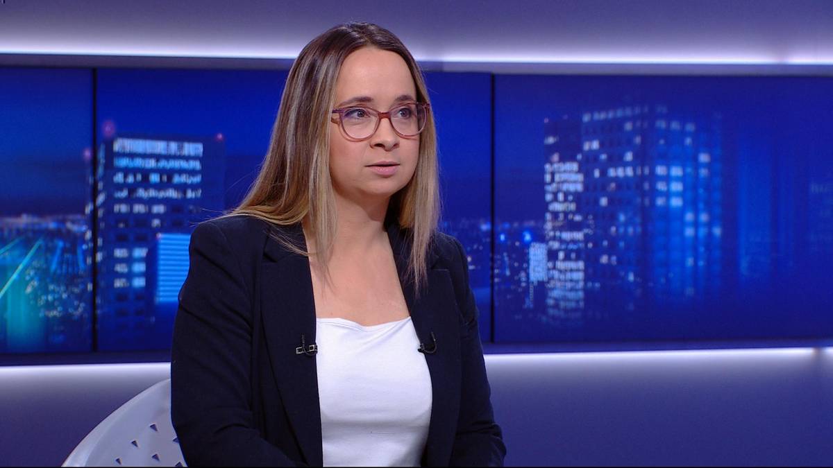 Kobieta w okularach i marynarce siedzi w studiu telewizyjnym.