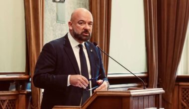 Mężczyzna w garniturze stoi przy m&oacute;wnicy i przemawia.