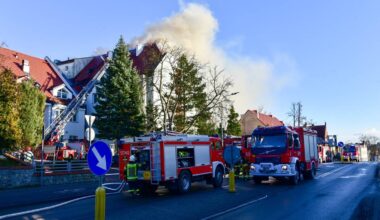 Samochody strażackie przy płonącym budynku, z kt&oacute;rego wydobywa się dym.