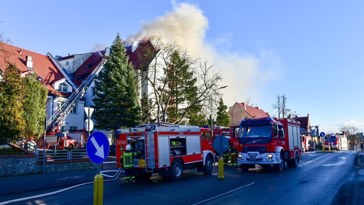 Samochody strażackie przy płonącym budynku, z kt&oacute;rego wydobywa się dym.