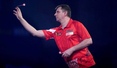 Krzysztof Ratajski w akcji, rzuca lotką do tarczy.