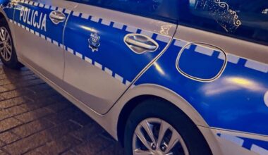 Fragment bocznej części radiowozu policyjnego z napisem "POLICJA" w kolorze niebieskim.