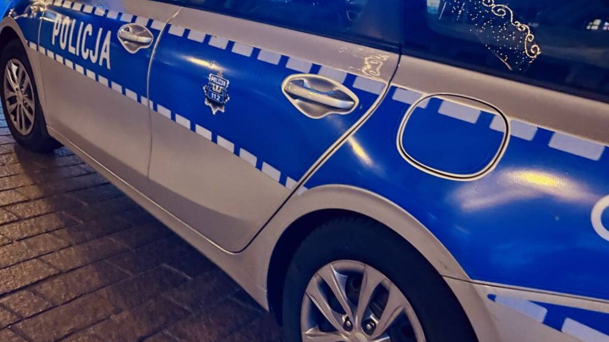 Fragment bocznej części radiowozu policyjnego z napisem "POLICJA" w kolorze niebieskim.