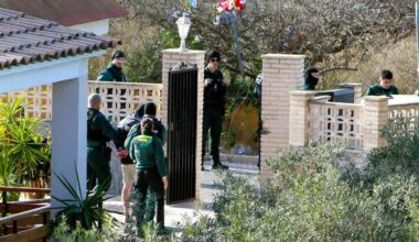 Policjanci w mundurach na terenie posesji otaczają mężczyznę w zielonym mundurze.