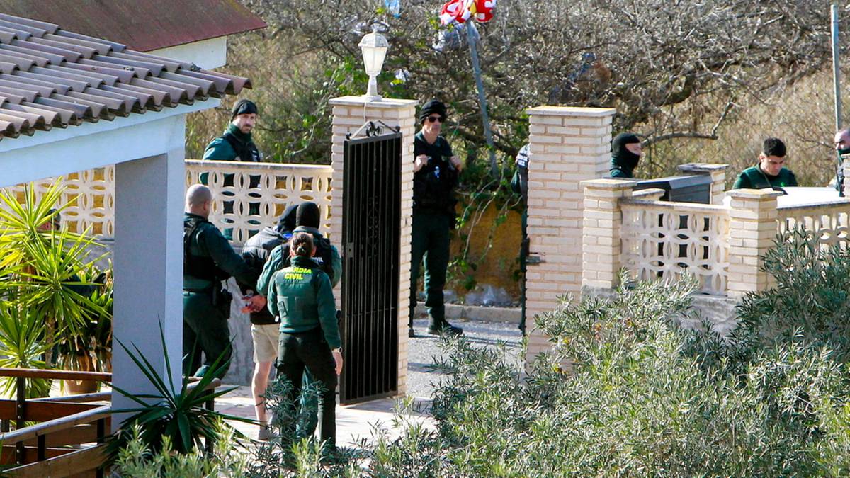Policjanci w mundurach na terenie posesji otaczają mężczyznę w zielonym mundurze.