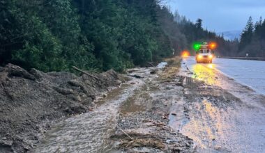 Droga zablokowana przez osuwisko błota i gruzu, z widocznym pojazdem służb ratowniczych.