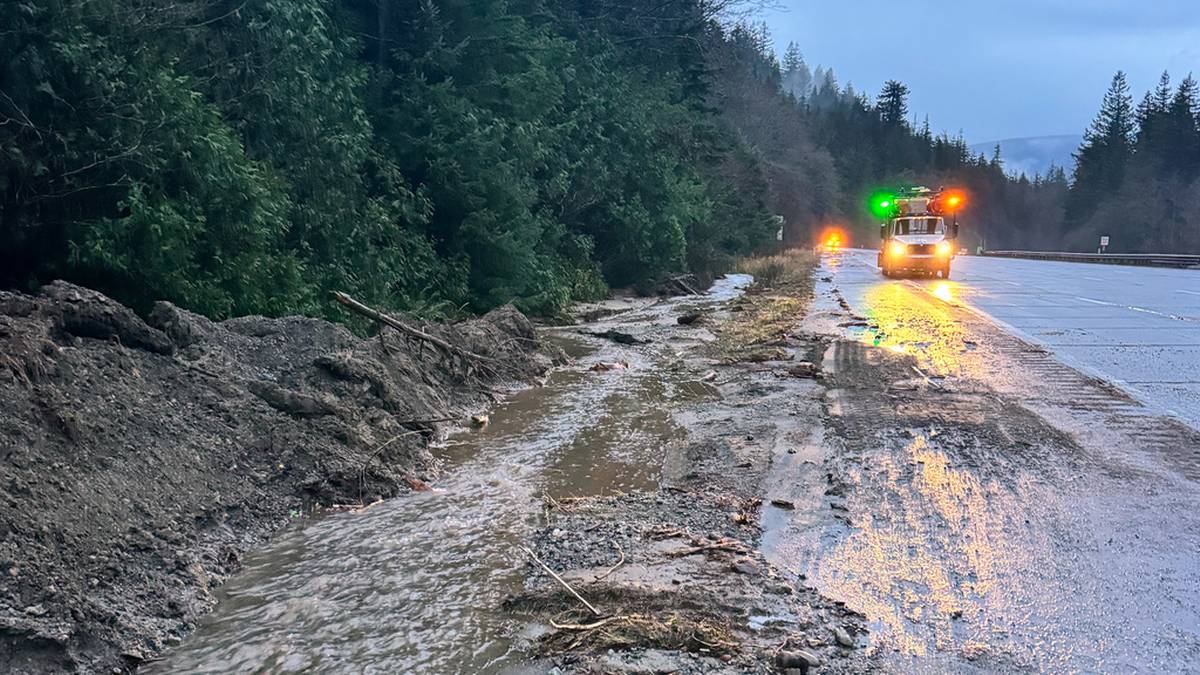 Droga zablokowana przez osuwisko błota i gruzu, z widocznym pojazdem służb ratowniczych.
