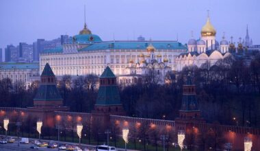 Widok na Kreml w Moskwie o zmierzchu, z widocznymi murami obronnymi i wieżami, a w tle budynki kremlowskie z kopułami.