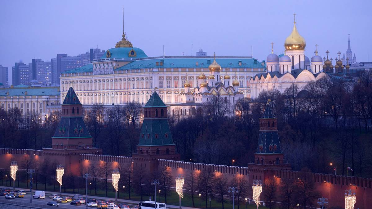 Widok na Kreml w Moskwie o zmierzchu, z widocznymi murami obronnymi i wieżami, a w tle budynki kremlowskie z kopułami.