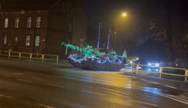Czołg Leopard I ozdobiony świątecznymi lampkami i łańcuchami jedzie nocą po ulicy.