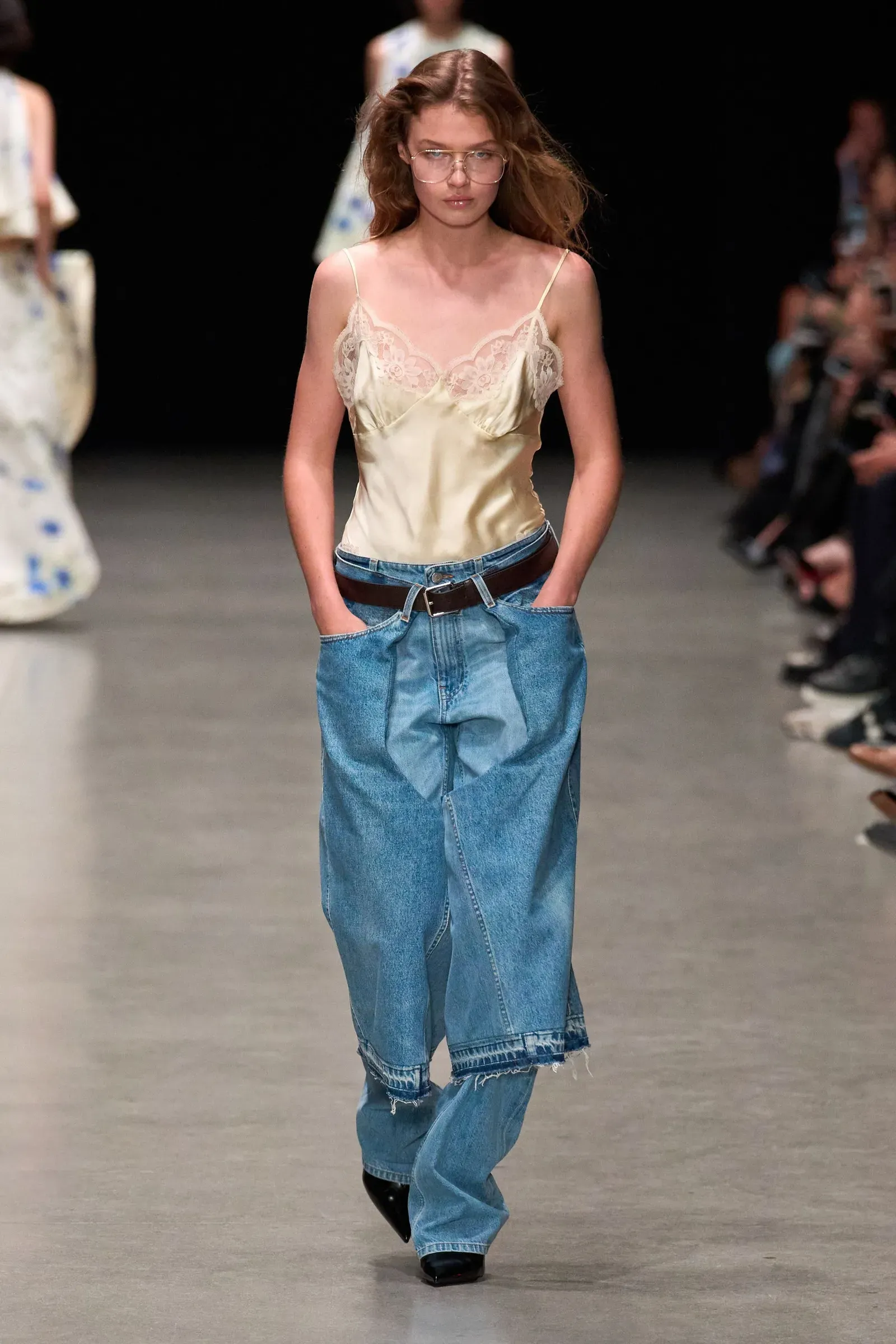 Modelka na wybiegu w luźnych, przerobionych dżinsach oraz satynowej bluzce na cienkich ramiączkach.