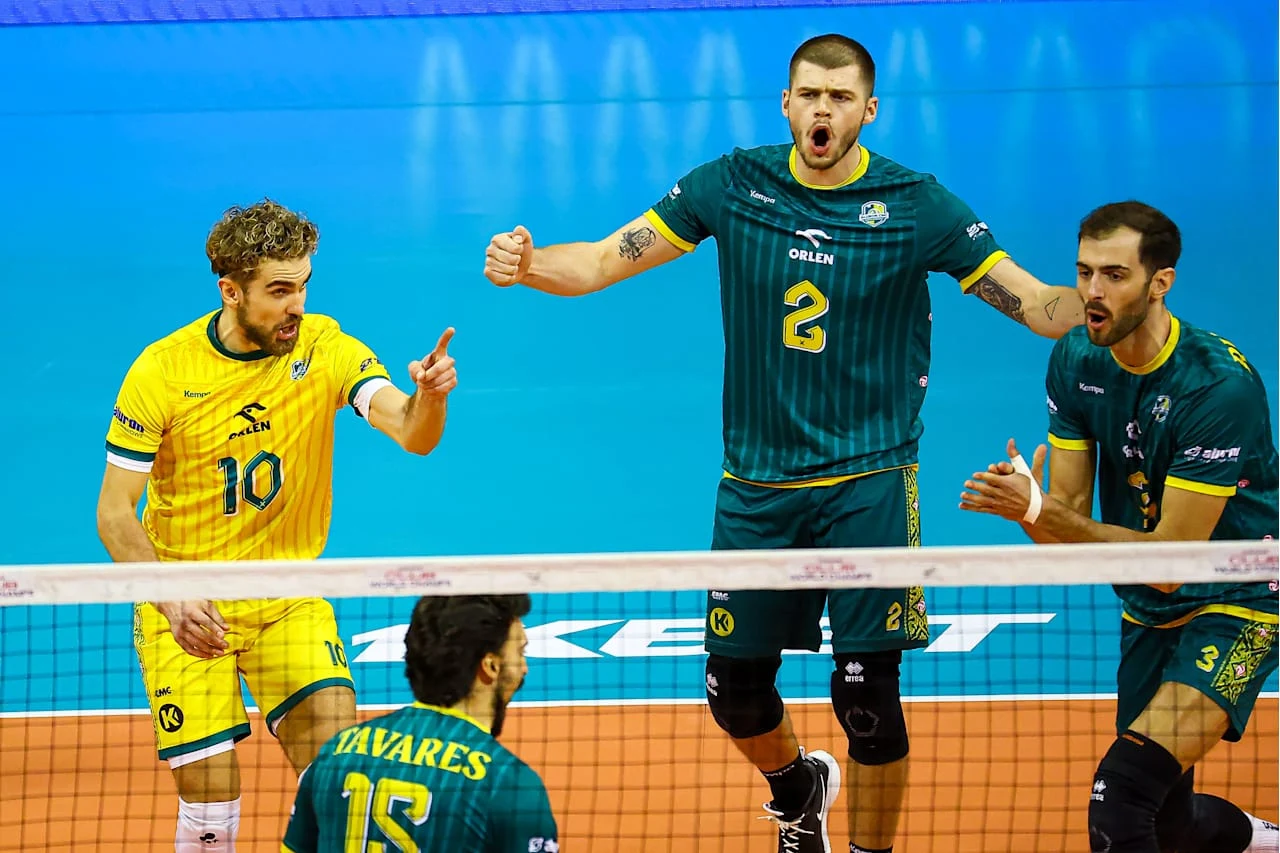 Grupa siatkarzy podczas meczu w wyrazistych zielonych i żółtych strojach sportowych, wyrażających intensywne emocje na boisku pod siatką w hali sportowej.