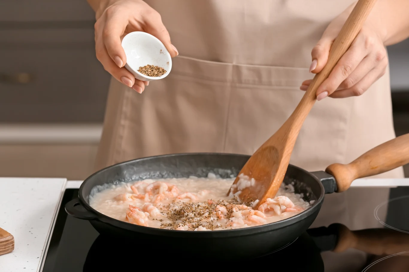 Tym zastąpisz sól w jedzeniu. Sposób by mniej solić i chronić zdrowie Dłoń osoby wsypującej przyprawy do patelni z duszonym kurczakiem w sosie, całość gotowana na kuchence indukcyjnej.