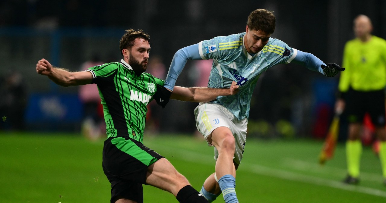 Grupa piłkarzy w jasnych strojach drużyny Juventus świętuje zdobycie bramki, jeden z zawodników jest mocno obejmowany przez kolegów z zespołu, wszyscy wyrażają radość i entuzjazm.