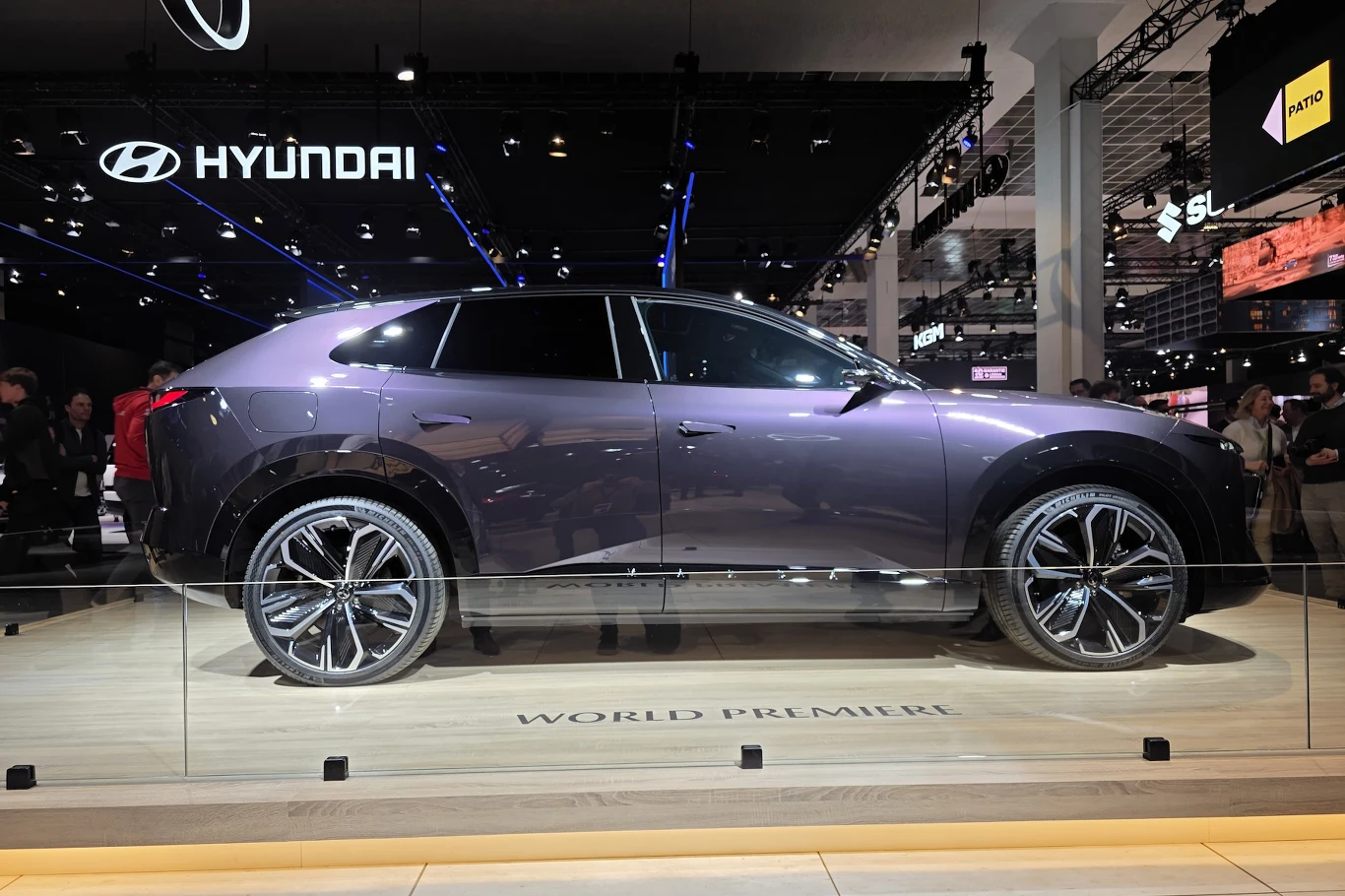 Mazda CX-6e Nowoczesny SUV marki Hyundai eksponowany podczas światowej premiery na targach motoryzacyjnych, otoczony przez szklaną barierę, oświetlony reflektorami z widocznymi logo producenta w tle.