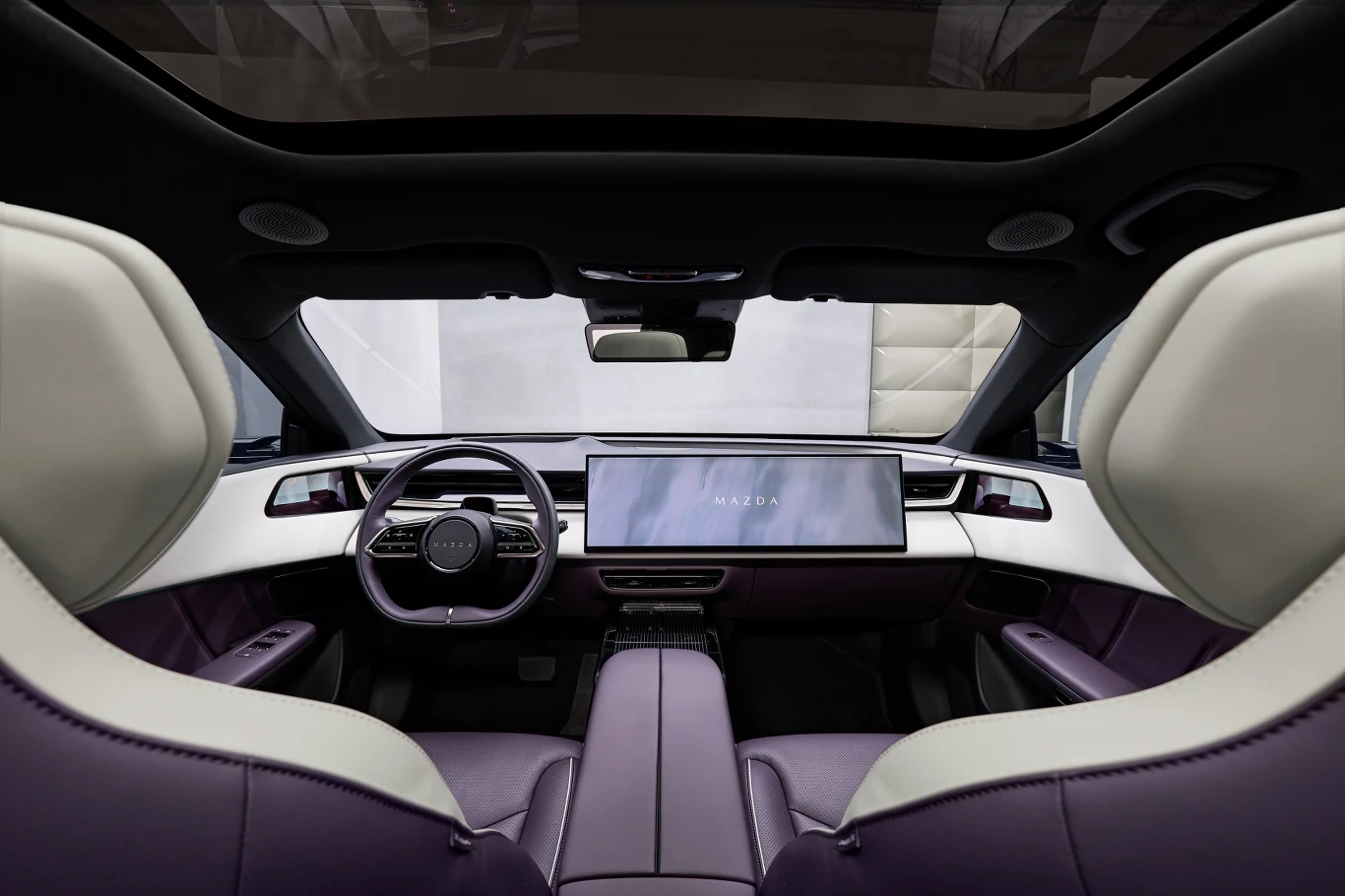 Mazda CX-6e Nowoczesne wnętrze luksusowego samochodu elektrycznego z dużym panoramicznym wyświetlaczem na desce rozdzielczej, elegancką kierownicą oraz dwukolorową tapicerką foteli.