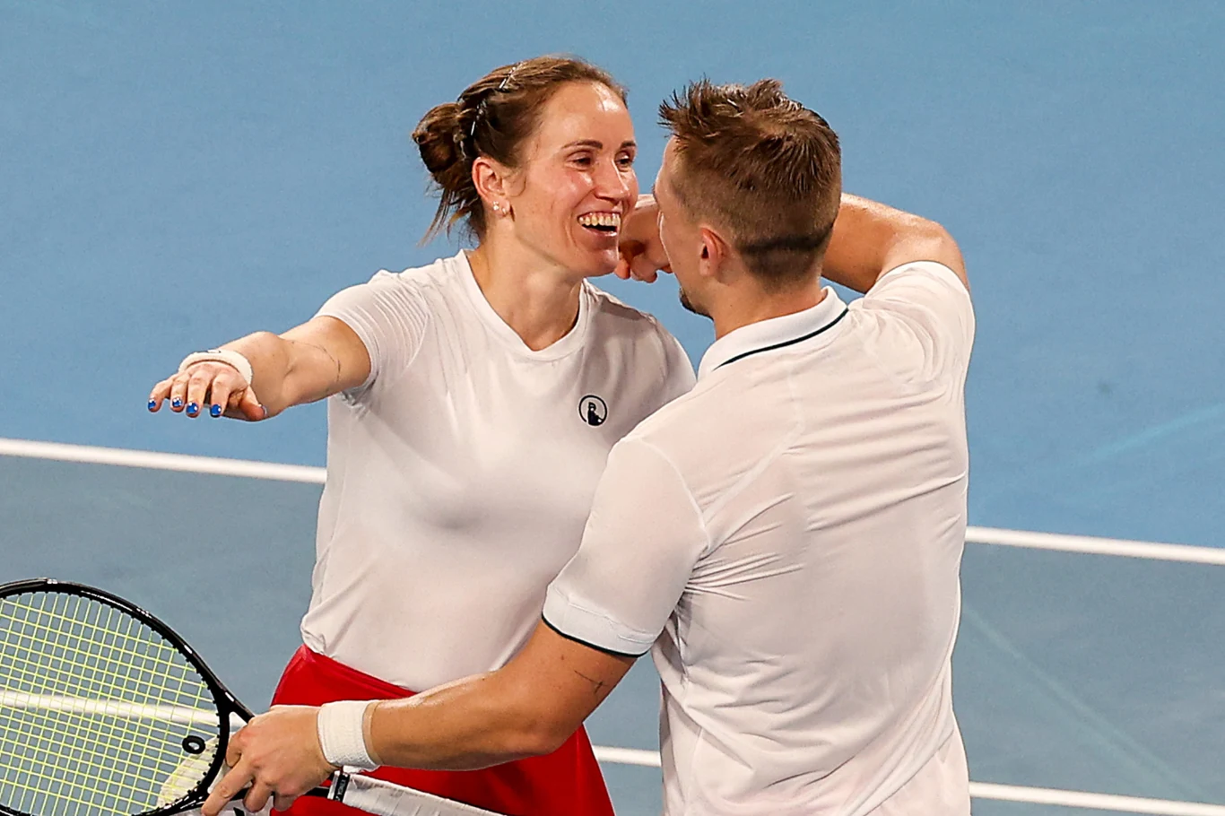 Dwoje tenisistów w sportowych strojach cieszy się ze zwycięstwa na korcie, uśmiechając się i obejmując po zakończonym meczu.