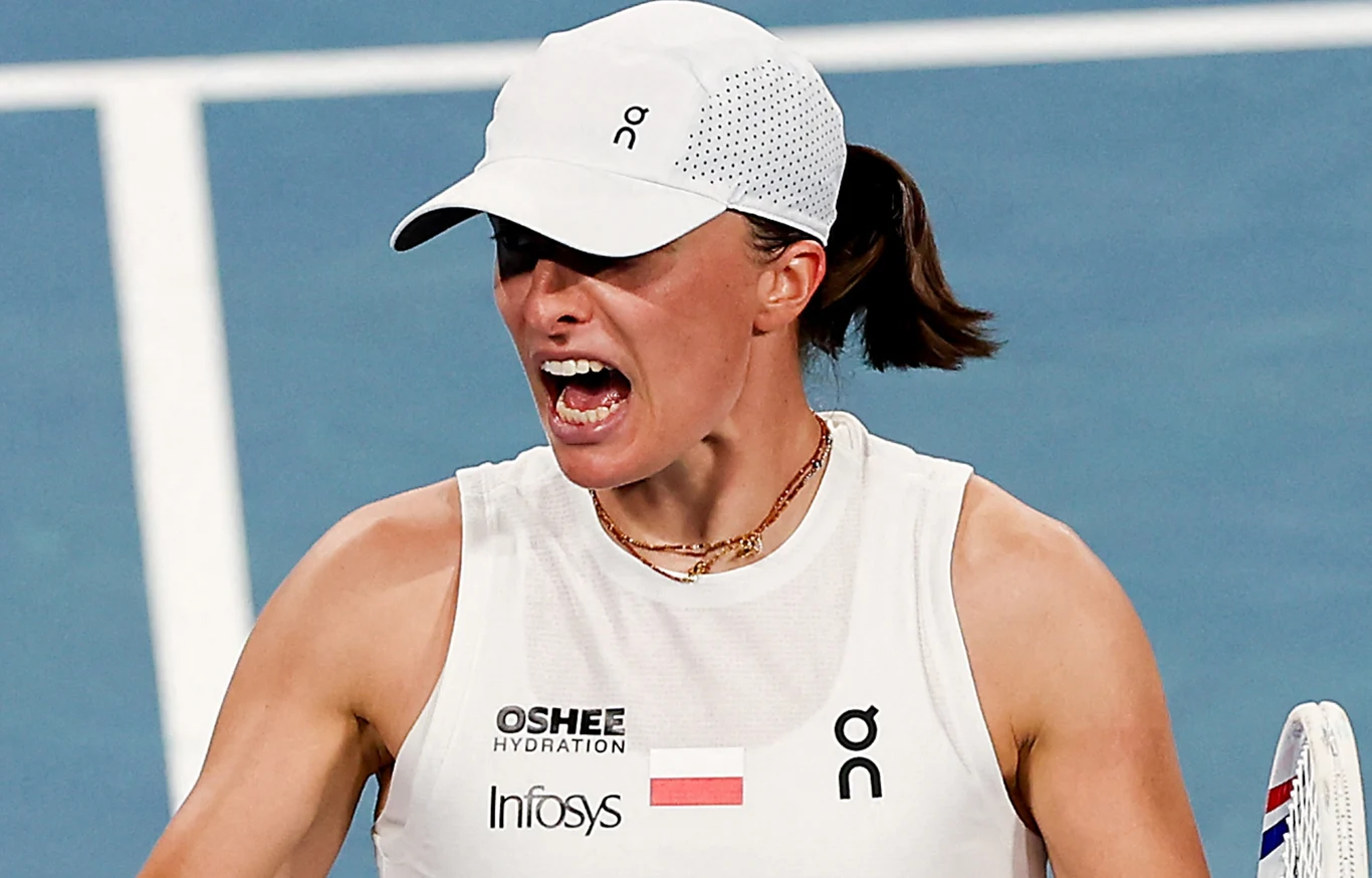 Iga Świątek, United Cup 2026 Zawodniczka tenisowa w białej koszulce i czapce sportowej wyraża silne emocje po zakończonej akcji na korcie tenisowym. W tle jasnoniebieska nawierzchnia kortu, widoczny fragment rakiety.