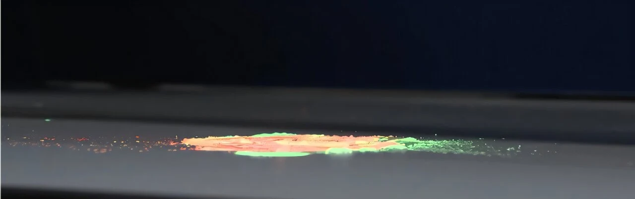 Kolorowy proszek rozproszony na płaskiej, jasnej powierzchni z przewagą zielonych i pomarańczowych odcieni, tło ciemne i jednolite.