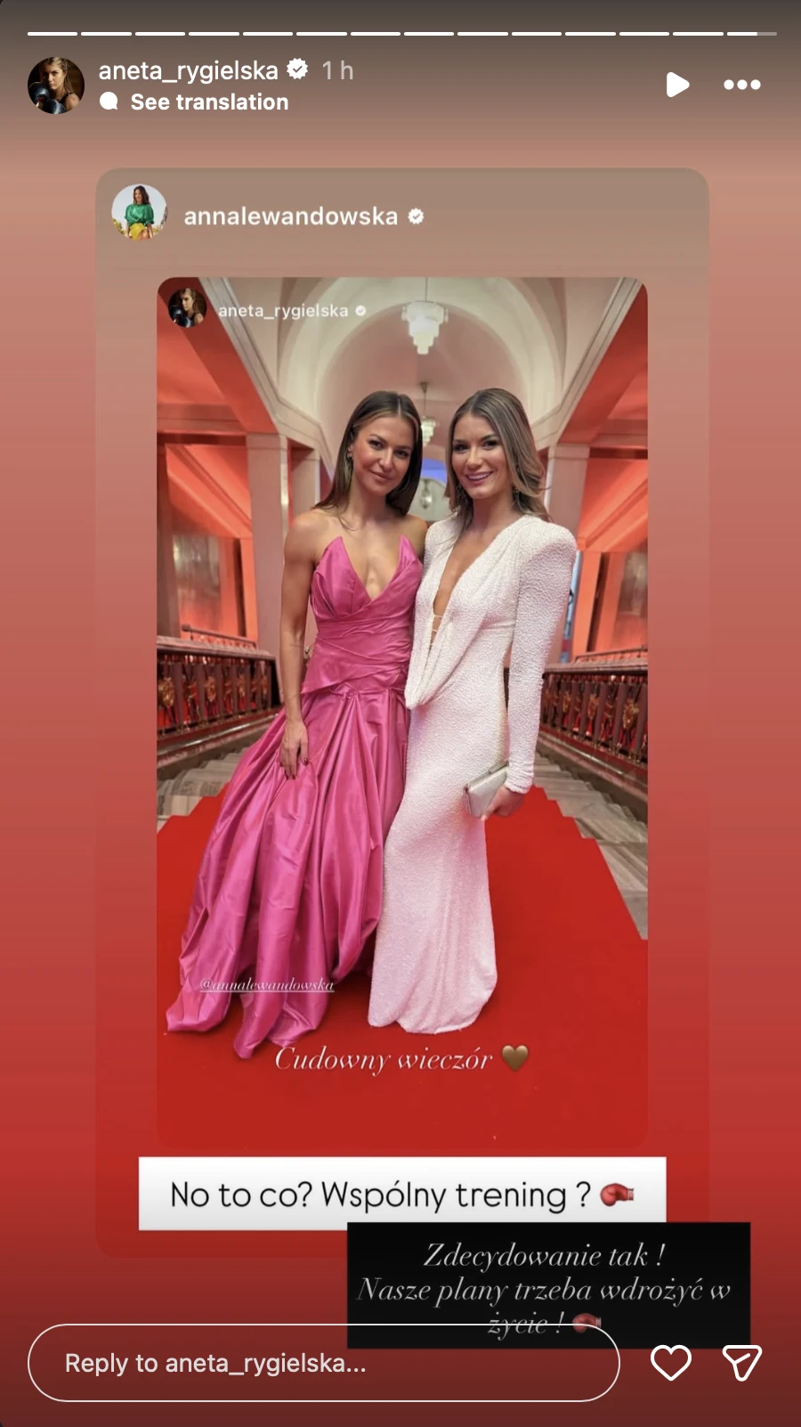 Dwie kobiety w eleganckich, wieczorowych sukniach pozują na czerwonym dywanie w luksusowym wnętrzu o wysokich łukach i kolumnach. U jednej z nich suknia jest pudroworóżowa, a u drugiej biała. Obie uśmiechnięte i pozujące w przyjacielskim geście.