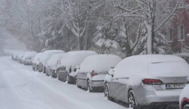 Rząd zaparkowanych samochod&oacute;w pokrytych grubą warstwą śniegu na ulicy.