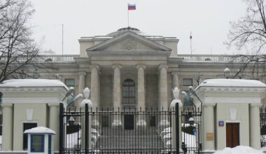 Budynek ambasady Rosji z flagą na dachu i ogrodzeniem przed wejściem, w zimowej scenerii.