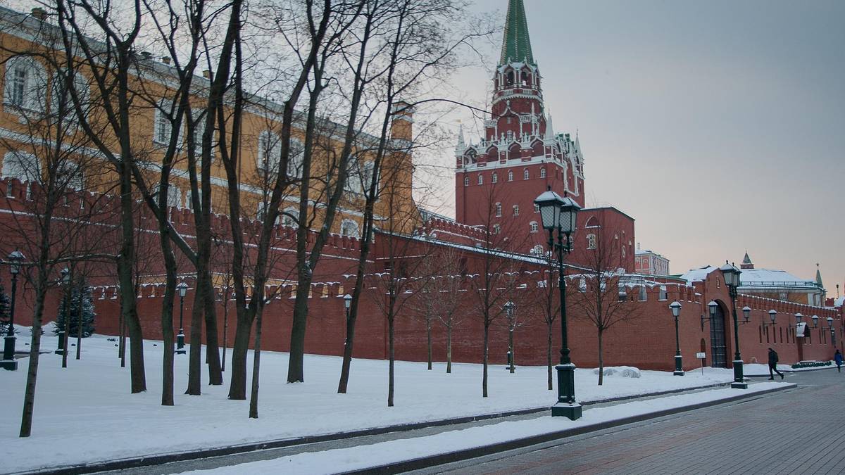 Zimowy widok na mury Kremla w Moskwie z czerwoną wieżą w tle, pokryte śniegiem.