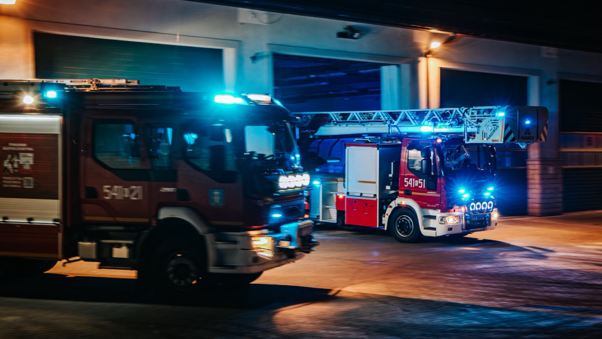 Dwa wozy strażackie z włączonymi światłami alarmowymi.