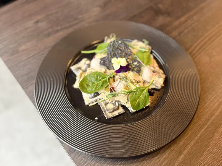 Pełnoziarniste czarne ravioli w sosie Alfredo, z żurawiną, młodym szpinakiem i parmezanem.