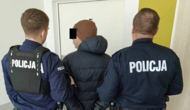 Policjanci prowadzą zatrzymanego mężczyznę w kajdankach.