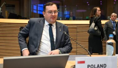 Minister rolnictwa Stefan Krajewski siedzi przy stole z laptopem i tabliczką "POLAND".