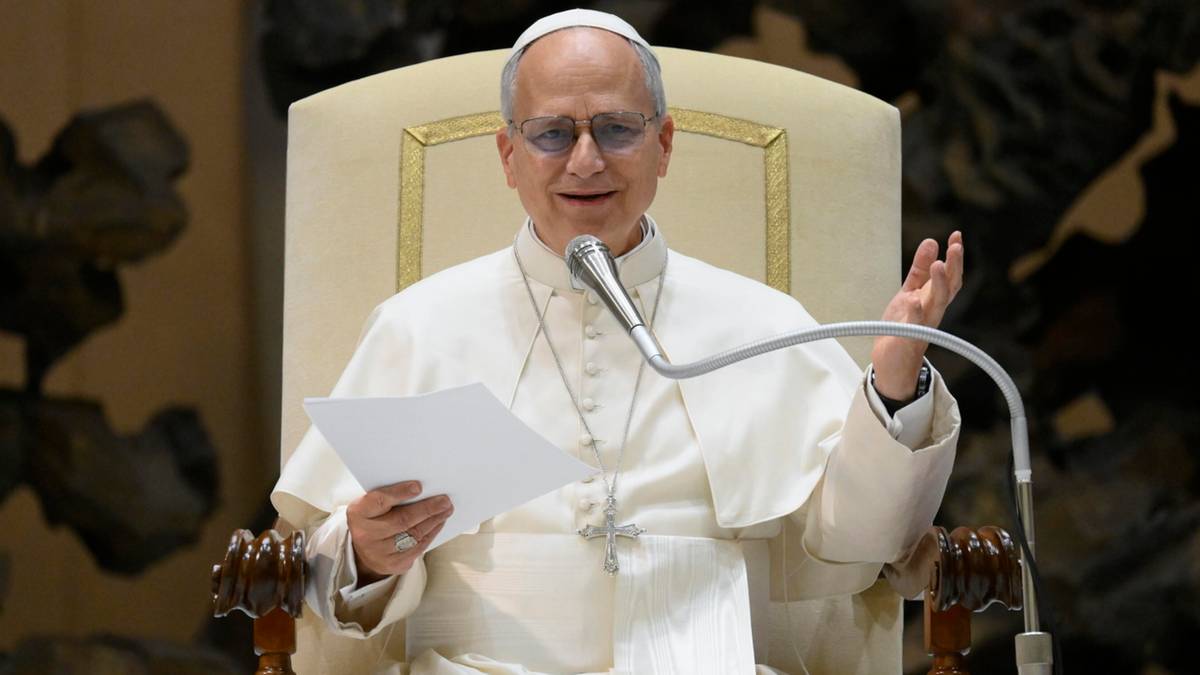 Papież Franciszek w białej szacie siedzi na tronie, czyta z kartki i przemawia do mikrofonu.