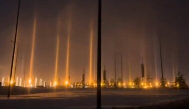 Słupy świetlne o pomarańczowej barwie unoszące się nad nocnym miastem.