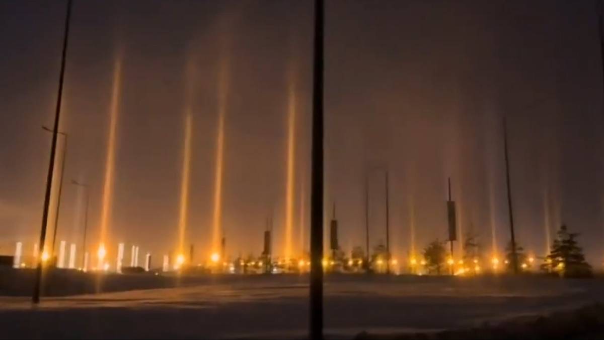 Słupy świetlne o pomarańczowej barwie unoszące się nad nocnym miastem.