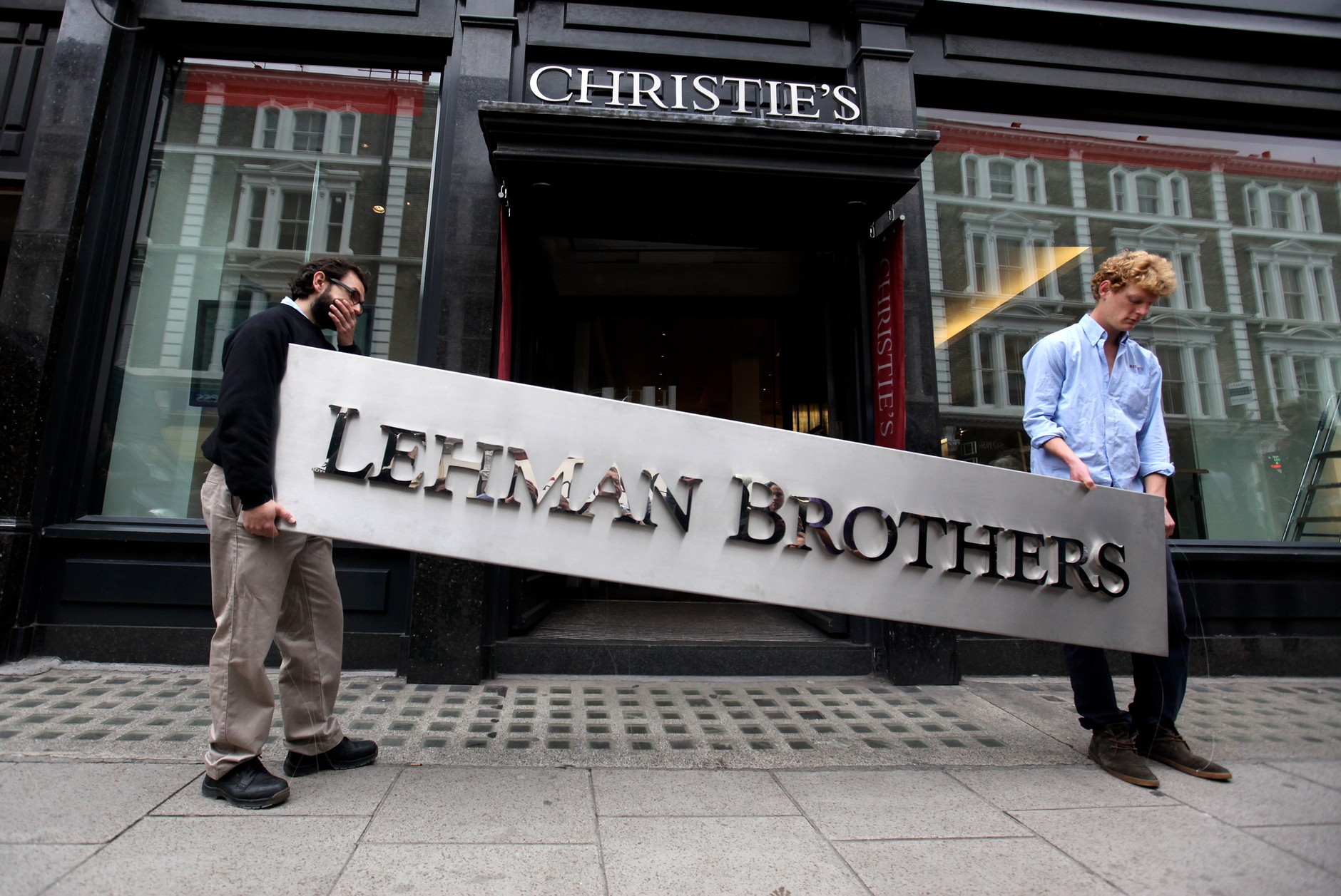 Dwóch pracowników domu aukcyjnego Christie's przenoszących tablicę z logo Lehman Brothers, Londyn, 24 września 2010 r. 