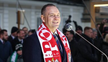 Prezydent Karol Nawrocki w szaliku biało-czerwonym z godłem Polski przemawia do zgromadzonego tłumu.