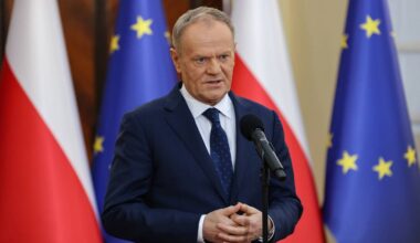 Premier Donald Tusk przemawia przed mikrofonem, w tle flagi Polski i Unii Europejskiej.