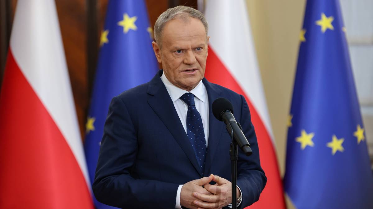 Premier Donald Tusk przemawia przed mikrofonem, w tle flagi Polski i Unii Europejskiej.