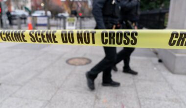 Dw&oacute;ch funkcjonariuszy policji przechodzi obok taśmy policyjnej "CRIME SCENE DO NOT CROSS"