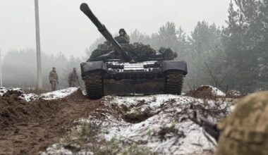 Czołg z żołnierzami na tle zimowego krajobrazu leśnego.