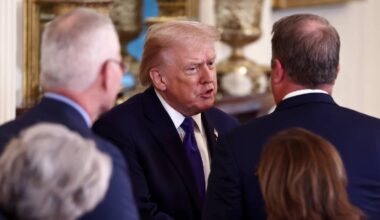 Donald Trump w garniturze i krawacie, otoczony przez kilka os&oacute;b, z kt&oacute;rymi rozmawia.