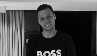 Młody mężczyzna w koszulce z napisem BOSS uśmiecha się do aparatu.