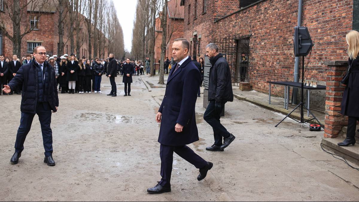 Prezydent Andrzej Duda w ciemnym garniturze i płaszczu, idący w kierunku widza, na tle grupy ludzi w czarnych płaszczach i budynk&oacute;w z cegły.