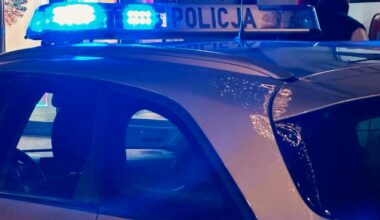 Tylna część radiowozu policyjnego z włączonymi niebieskimi sygnałami świetlnymi.