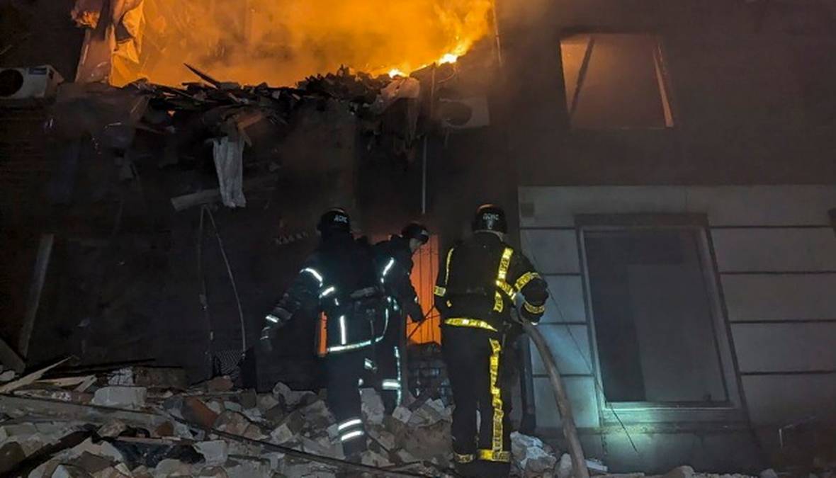 Strażacy w kamizelkach odblaskowych w pobliżu zniszczonego budynku mieszkalnego.