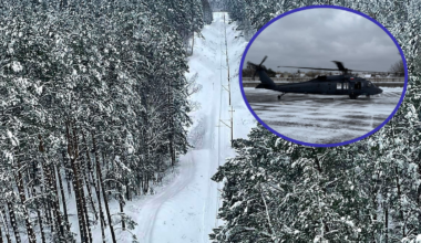 Policyjny śmigłowiec Black Hawk wylądował na tle zimowego krajobrazu z zasypanymi śniegiem drzewami i torami kolejowymi.