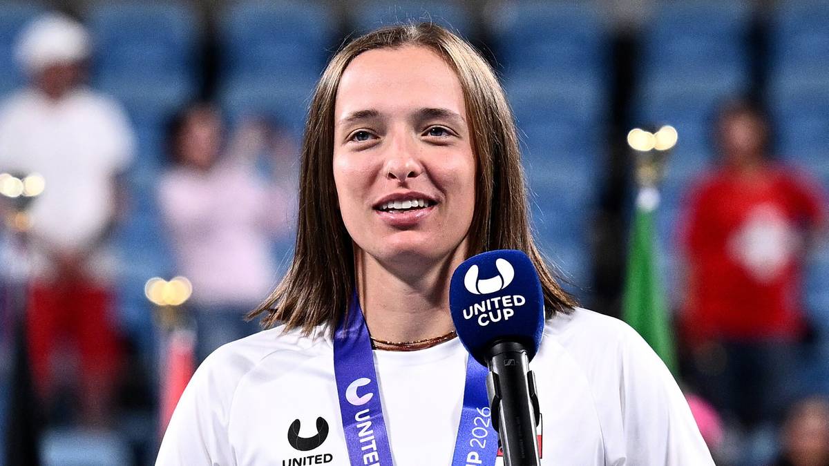 Iga Świątek z pucharem i medalem po wygranym meczu, obok mikrofonu.