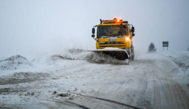 Ż&oacute;łty pług śnieżny z włączonymi światłami ostrzegawczymi usuwa śnieg z zaśnieżonej drogi.