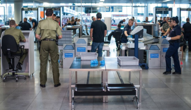 Kontrola bezpieczeństwa na lotnisku z celnikami i podr&oacute;żnymi przechodzącymi przez bramki.
