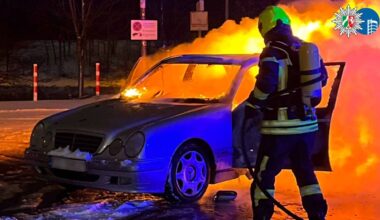 Samoch&oacute;d osobowy objęty płomieniami, obok strażak w akcji.